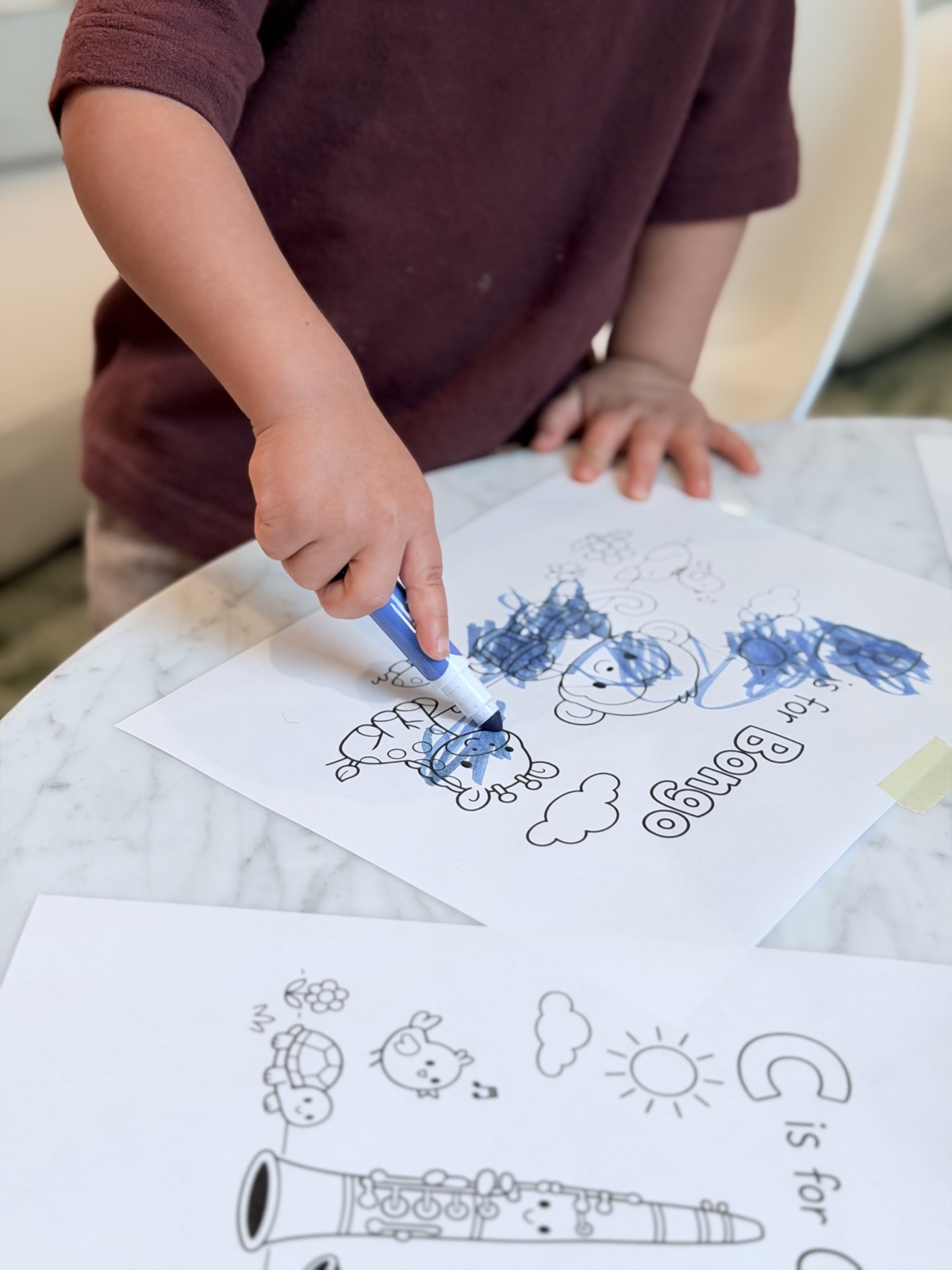 A child coloring a Colorín letter page with a blue marker